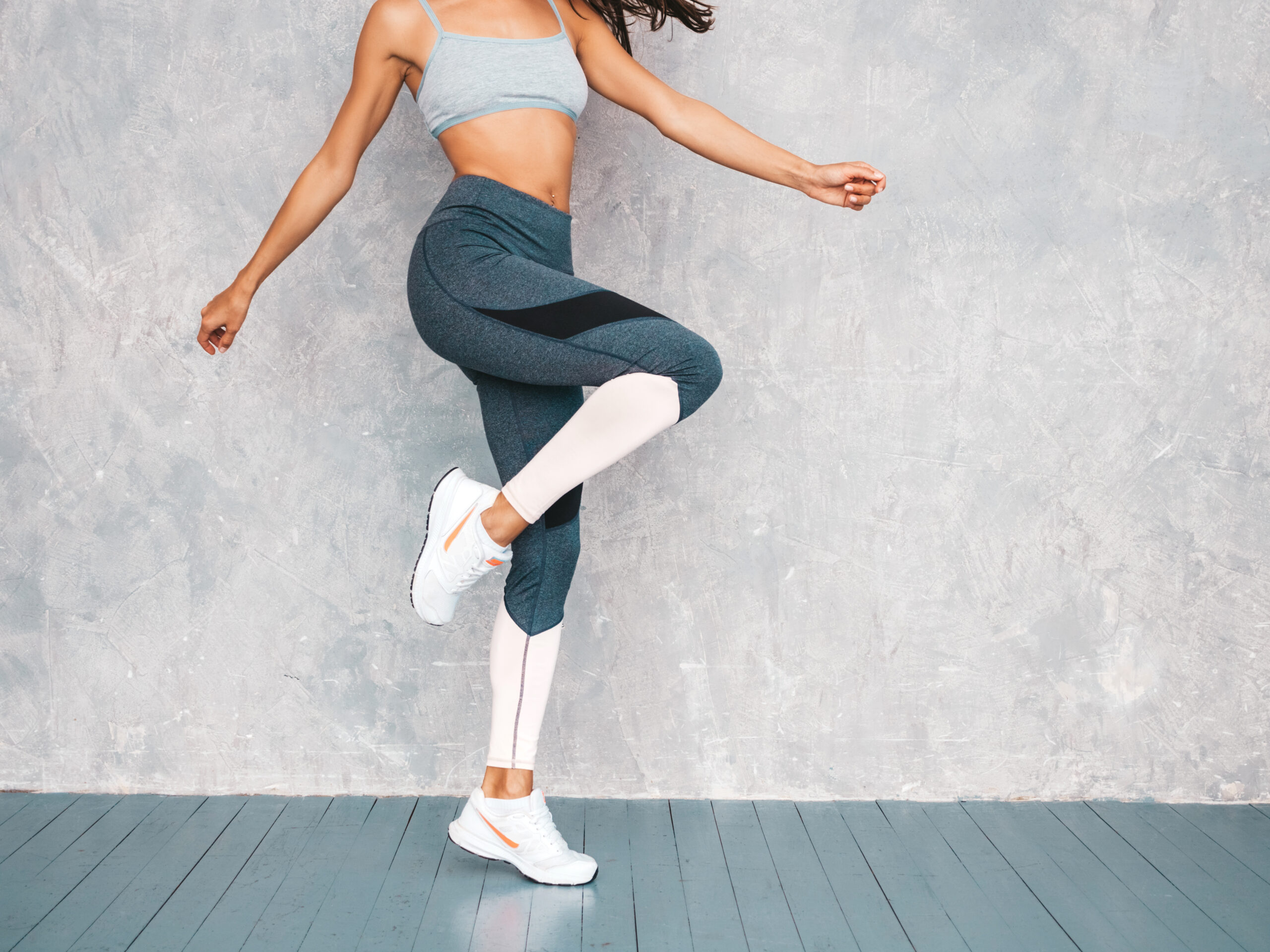 Portrait of confident fitness woman in sports clothing looking confident.Young female wearing sportswear. Beautiful model with perfect tanned body.Female jumping in studio near gray wall Baby Blue Gym Set